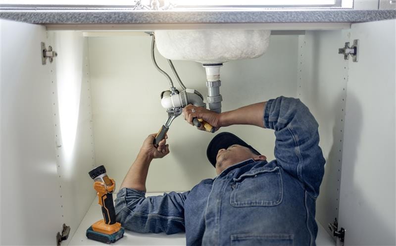 Plumber repairing pipes beneath a bathroom sink in Palo Alto